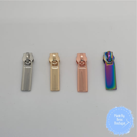 Image shows four #5 zipper pulls. They are straight and plain in shape, The colours shown left to right are silver, gold, rose gold and rainbow.